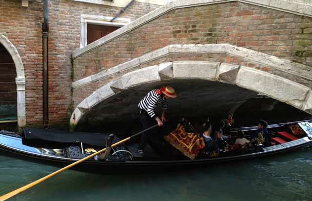 Gondolier ducking under a low bridge